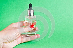 Female hand holding bottle of moisturizing face oil on a  green background. A professional product for the perfect complexion. Wom