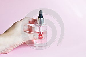 Female hand holding bottle of moisturizing face oil on a pink background. A professional product for a perfect complexion. Women`s