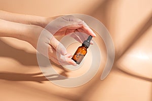 Female hand holding a bottle with serum for face care. Daily routine and treatment for the skin. Mockup for your design.