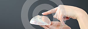 Female hand holding breast implant and pointing finger at it closeup
