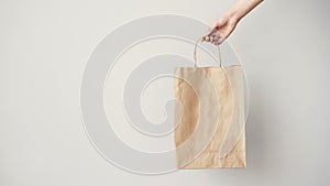 Female hand holding brown paper bag on grey background