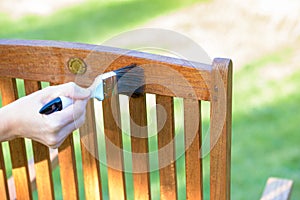 female hand holding a brush applying varnish paint on a wooden garden chair - painting and caring for wood