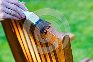 female hand holding a brush applying varnish paint on a wooden garden chair- painting and caring for wood