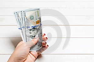Female hand holding a bundle of one hundred dollar banknotes on wooden background. Salary and wage concept with copy space
