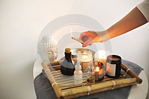 Female hand holding burning incense over wicker bamboo tray with candles and various oils in SPA