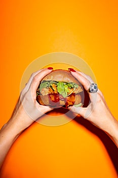 Female hand holding chicken burger against orange background.