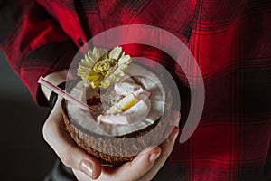 Female hand holding a coconut cocktail with berries and flower