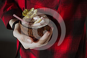 Female hand holding a coconut cocktail with berries and flower