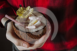 Female hand holding a coconut cocktail with berries and flower
