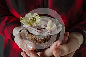 Female hand holding a coconut cocktail with berries and flower