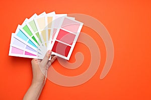 Female hand holding color palettes on orange background