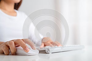 Female hand holding computer wireless mouse and working on a computer keyboard. work at home concept