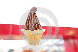 A female hand holding a cone of soft chocolate ice cream on red building background
