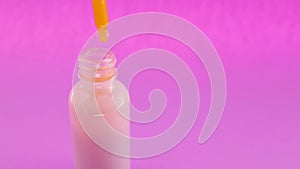 Female hand holding cosmetic pipette with natural remedy in a glass bottle on a pink background.