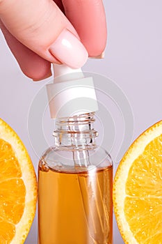 Female hand holding a dropper of a Bottle with cosmetic serum and citrus fruit slices. Skin care concept