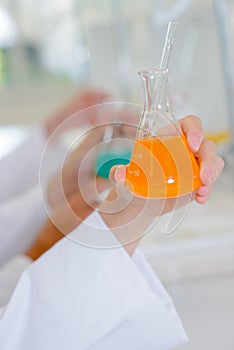 Female hand holding flask containing orange liquid