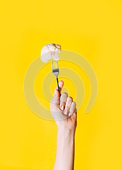 Female hand holding fork and cauliflower on it on yellow background.