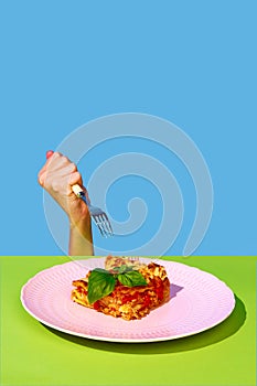 Female hand holding fork over delicious Italian food, lasagna over green and blue background