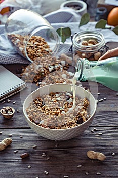 Female hand holding glass bottle pouring milk in cereal granola flakes bowl