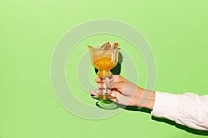 Female hand holding glass with orange juice cocktail with vodka on light green background. Concept of alcohol, drinks