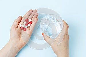 Female hand holding glass of water and pills, top view