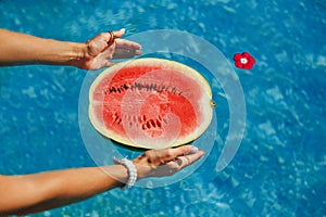 Female hand holding half of ripe juicy watermelon in the swimming pool. Freshness, Enjoyment Concept