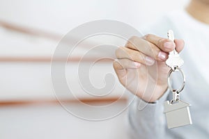 Female hand holding house key on home shaped key chain. concept for buying real estate agent