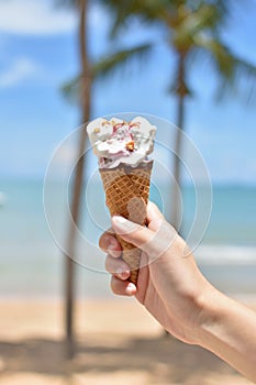 Female hand holding ice cream in waffle cone against summer beach background