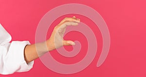 Female hand holding invisible object over pink background