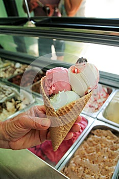 Female hand is holding a large strawberry, mint, vanilla with sour cherry ice cream in waffle cone.