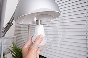 Female hand holding a led light bulb to change, replace it at home, screwing in the bulb into a lamp holder for energy saving and