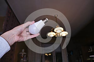 Female hand holding a led light bulb to change, replace it at home, screwing in the bulb into a lamp holder for energy saving and