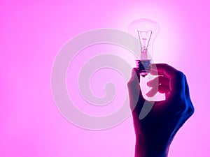 Female hand and holding luminous light bulb. Electric incandescent light bulb in hand on purple background. Inspiration Ideas conc