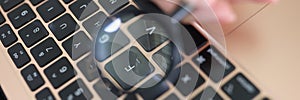 Female hand holding magnifying glass above laptop keyboard