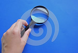 Female hand holding  Magnifying glass  isolate on a blue backgroun
