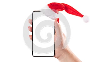 Female hand holding mobile smart phone with santa hat isolated on white background. Blank white screen. Concept of Christmas