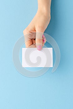 Female hand holding a mockup of a business card on blue background.