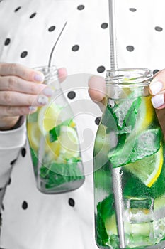 Female hand holding Mojito refreshing cocktail with eco metal drinking straw, alcohol drink. Lemonade with lemon and