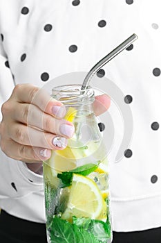 Female hand holding Mojito refreshing cocktail with eco metal drinking straw, alcohol drink. Lemonade with lemon and