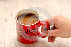 Female hand holding a mug of coffee on wooden background