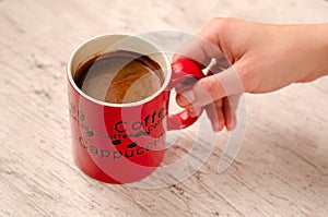 Female hand holding a mug of coffee on wooden background