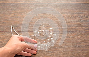 Female hand holding a necklace of glass on wooden background.