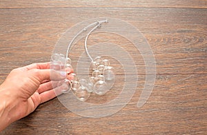 Female hand holding a necklace of glass on wooden background.