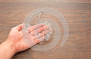 Female hand holding a necklace of glass on wooden background.