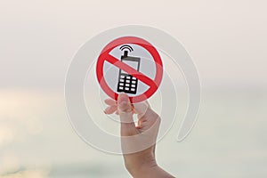 Female hand holding No phone calls sign on the beach