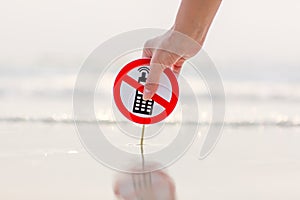 Female hand holding No phone calls sign on the beach