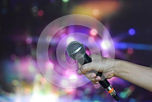A female hand is holding one microphone against the colorful lights