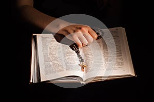 Female hand holding opened holy bible and crucifix.