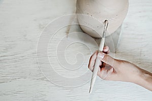 Female hand holding paint brush next to clay vase in hobby workshop