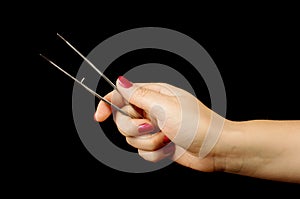 Female hand holding pair of metal tweezers on the black background